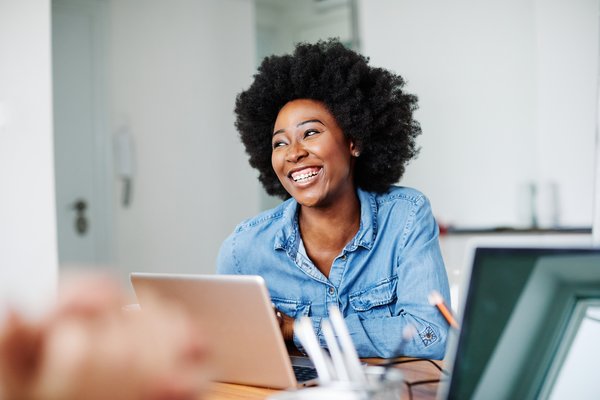 Image shows a woman sat in front of a laptop smiling to someone off camera.