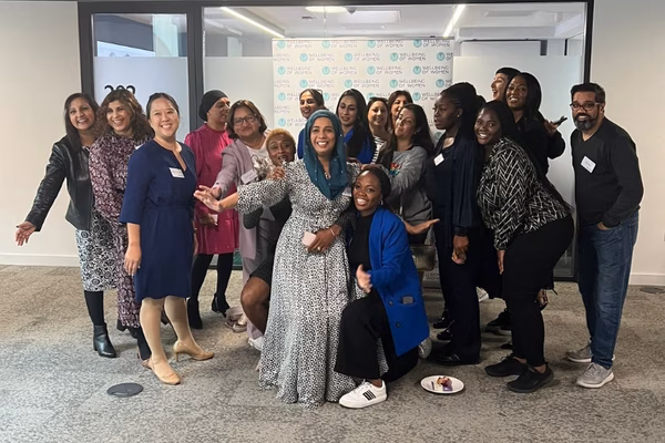 A group of women standing huddle together, there is also one man standing on the far right side- Dr Nighat Arif is in the centre; arms outstretched