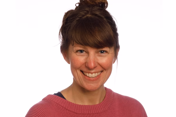 Sara Cumming is smiling broadly at the camera wearing a pink jumper