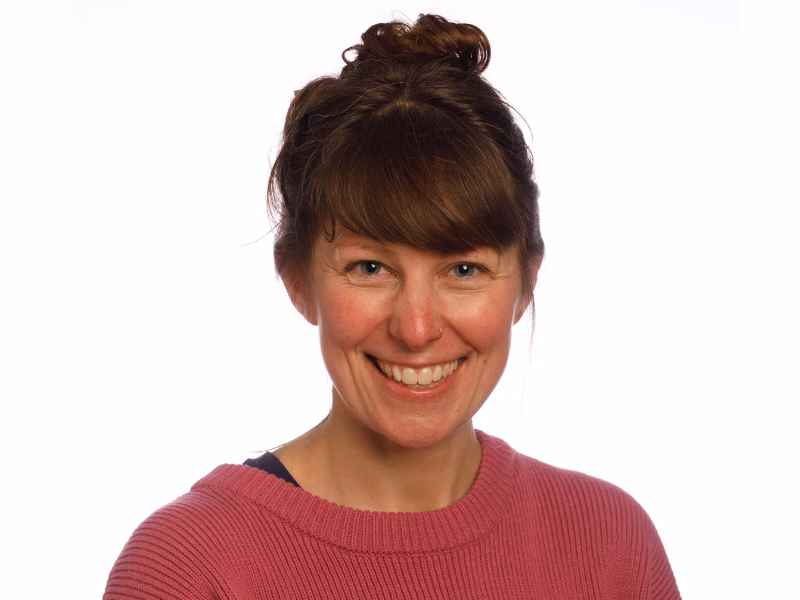 Sara Cumming is smiling broadly at the camera wearing a pink jumper