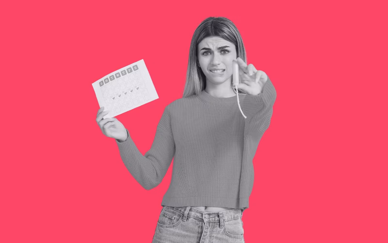 A teenager holding a menstrual calendar and tampon looking ocnfused.