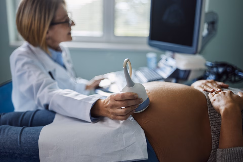 Ultrasound being conducted on a late stage pregnancy, bump is large in foreground and healthcare professional is blurred in background