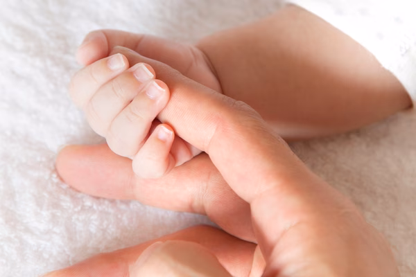 A mother holds the hand of her baby