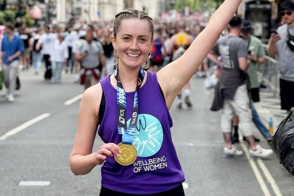 Researcher Marianne Watters holds a running medal smiling in Wellbeing of Women t-shirt
