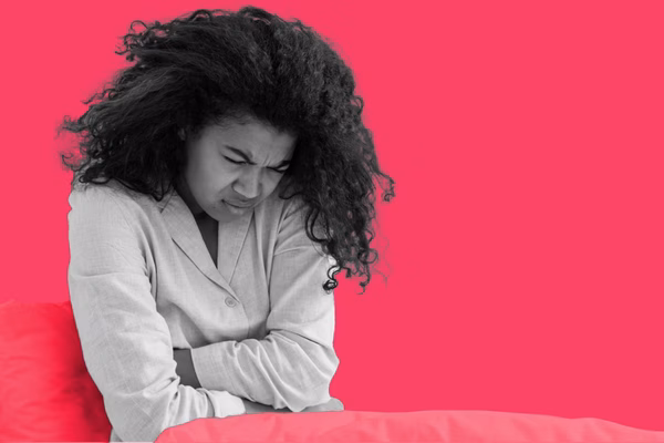 A women hunched over in pain, with her arms across her stomach.