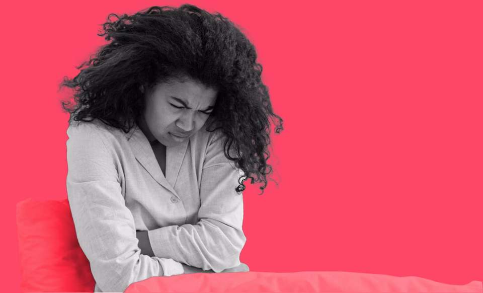 A women hunched over in pain, with her arms across her stomach.