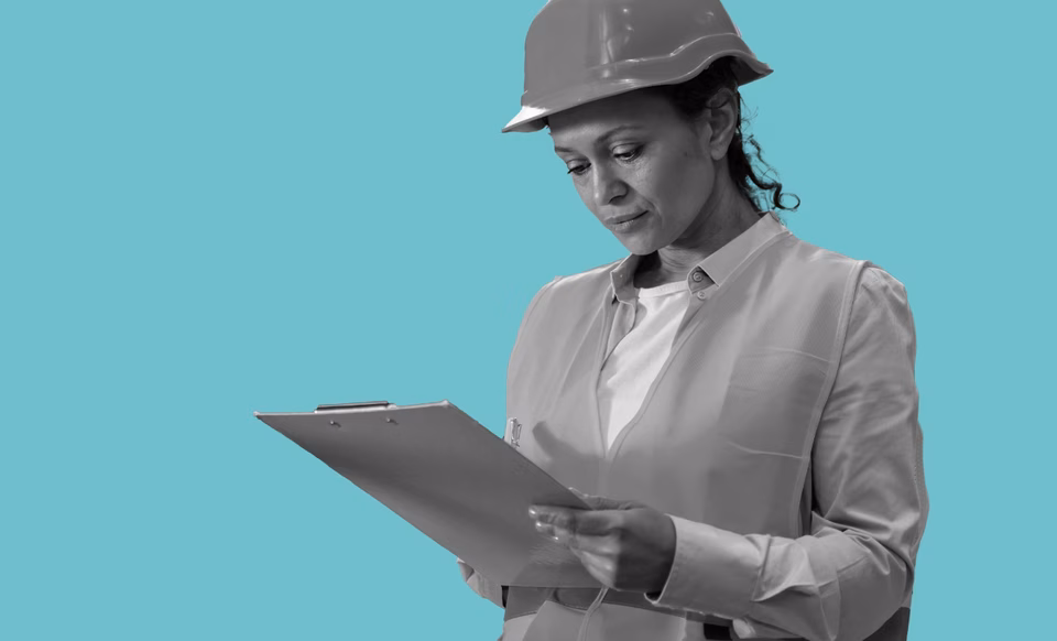A women wearing a hard hat looking at a clipboard.